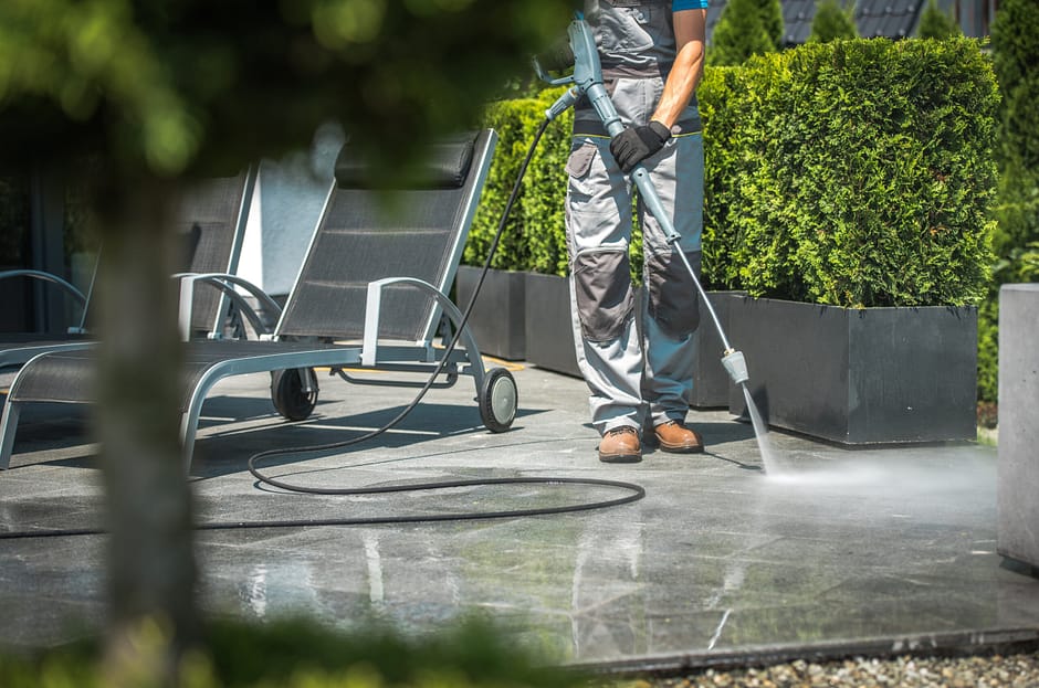 Worker performing outdoor pressure washing service on a patio area